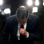 Comey bends over, with a wall of lights behind him.