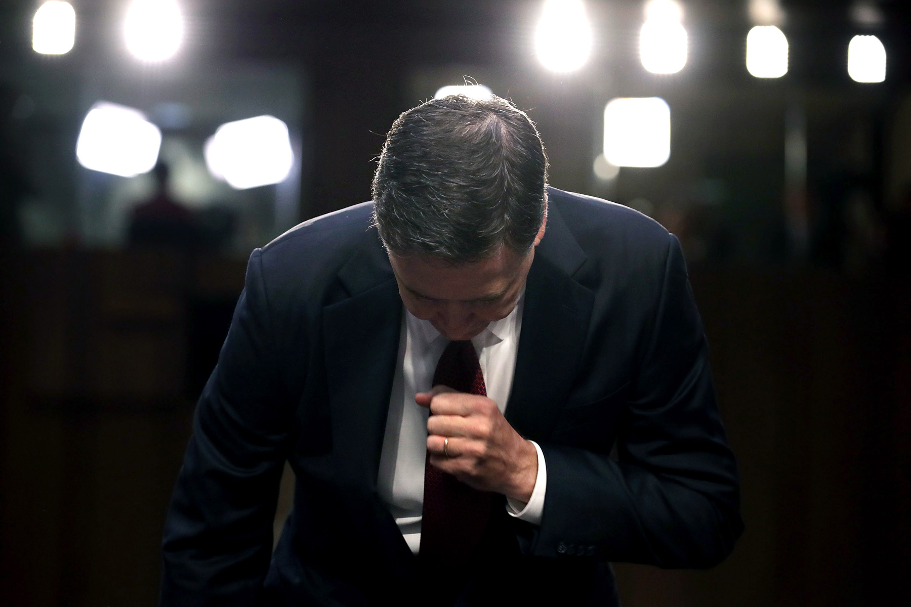 Comey bends over, with a wall of lights behind him.