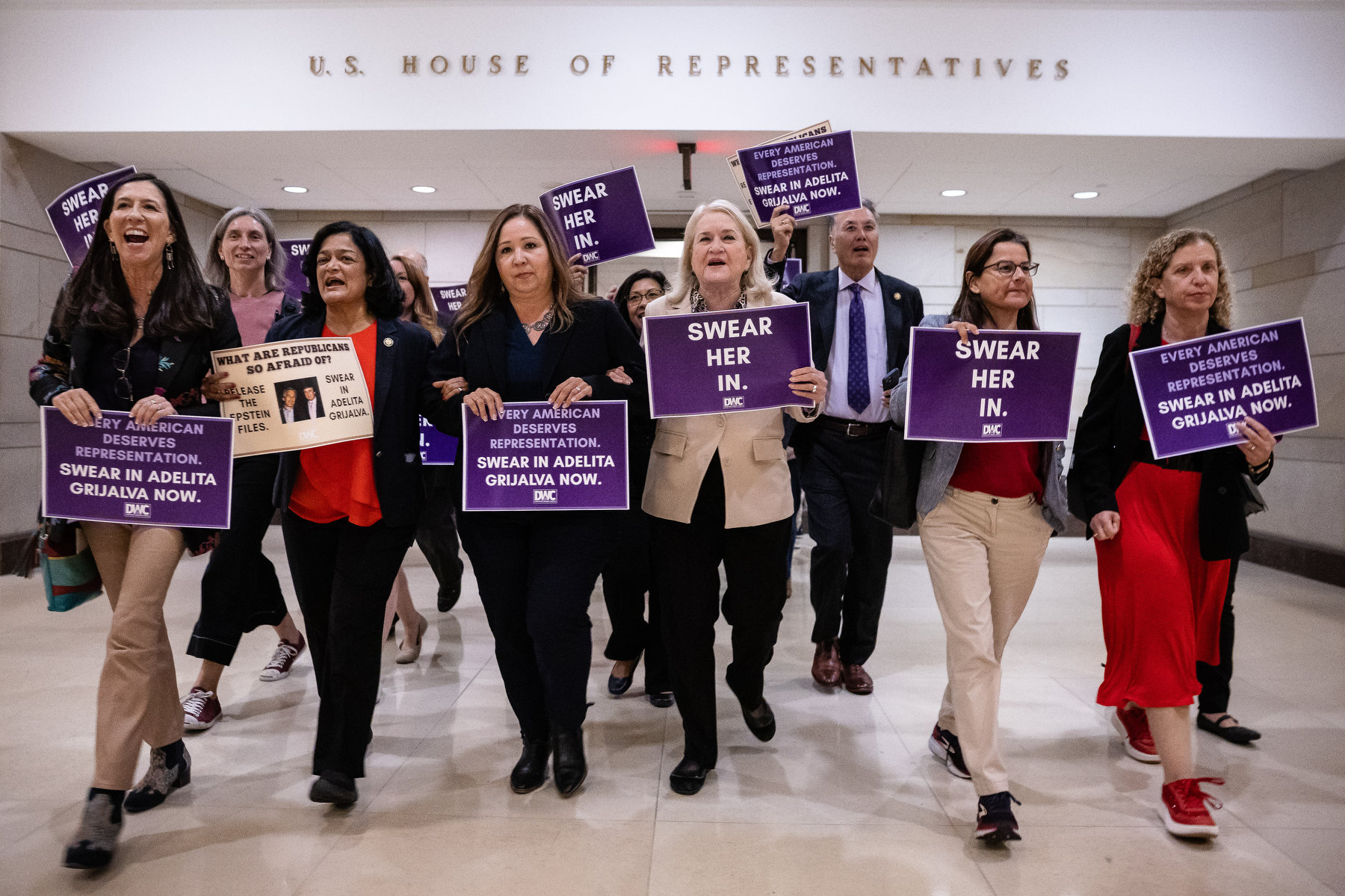 A group of people walk with signs saying "swear her in" through the Capitol building.