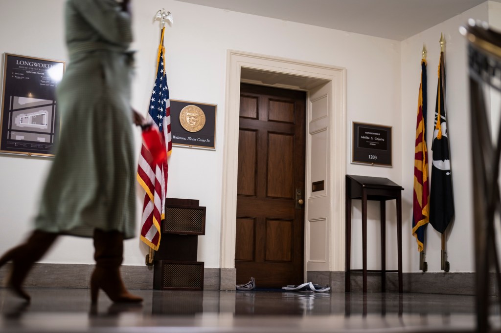 A person walks by a closed office door where papers sit, piling up.
