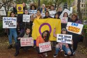A group of people look at the camera while holding intersex rights signs.