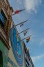 Colorful flags and a mural on the exterior of a building under a blue sky.