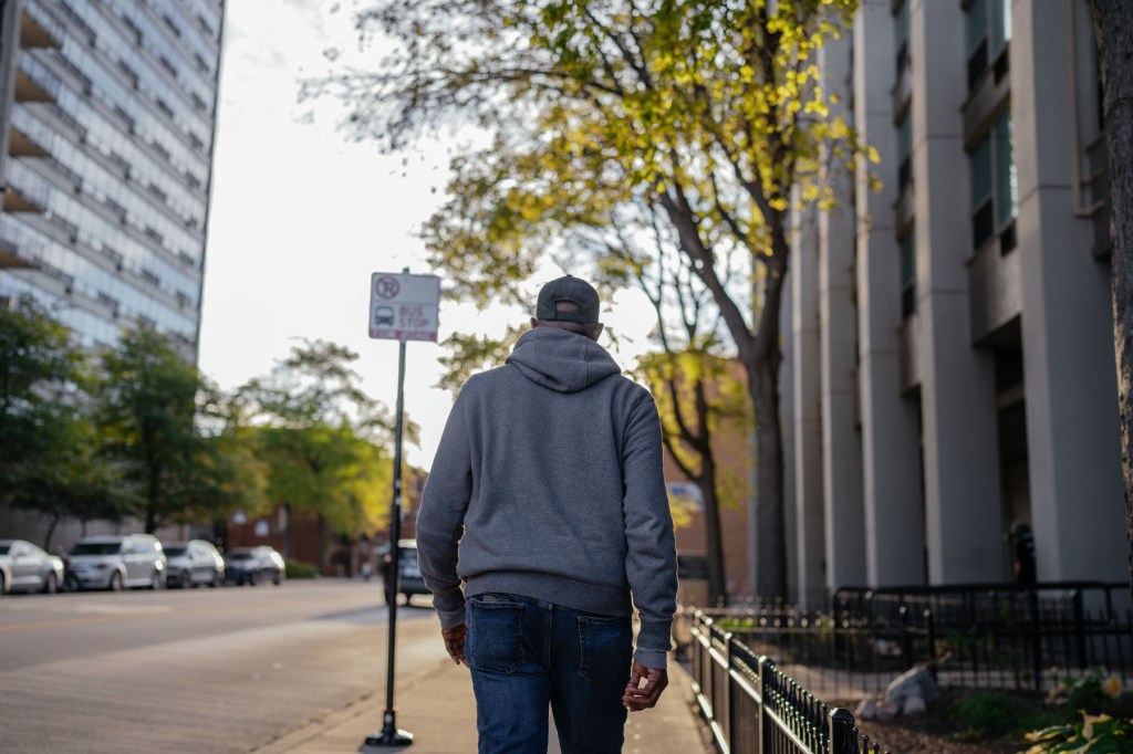 Rear view of a man in a gray hoodie and jeans walking along a tree-lined street on Chicago’s North Side.