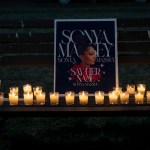 Candles light a sign for Sonya Massey propped up on a bench.