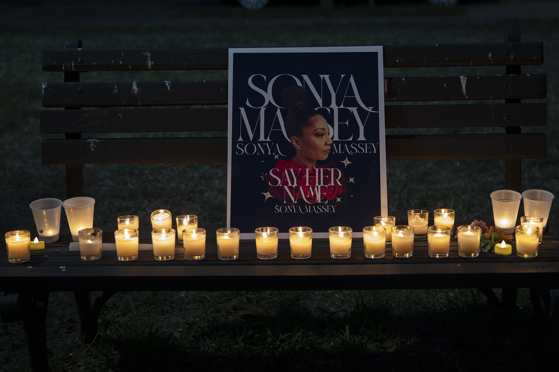 Candles light a sign for Sonya Massey propped up on a bench.