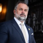 Cory Mills stands in a doorway in a suit.