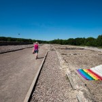A woman walks past a rainbow flag and plaque siting alongside a gravel road.