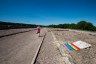 A woman walks past a rainbow flag and plaque siting alongside a gravel road.
