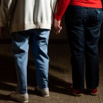 Two older women hold hands in the hallways of a community for older adults.
