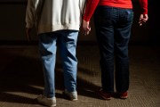 Two older women hold hands in the hallways of a community for older adults.