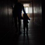 A parent leads a child down a dark hallway.