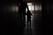 A parent leads a child down a dark hallway.