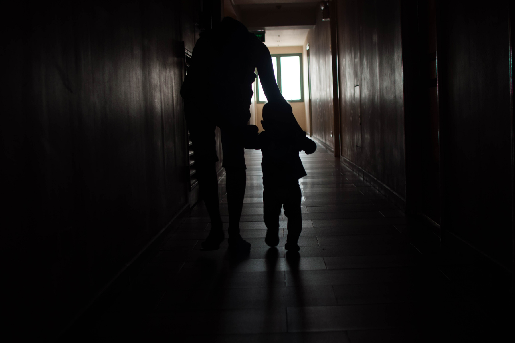 A parent leads a child down a dark hallway.