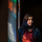 A portrait of a woman whose face is lit up by light through a church stained glass window.