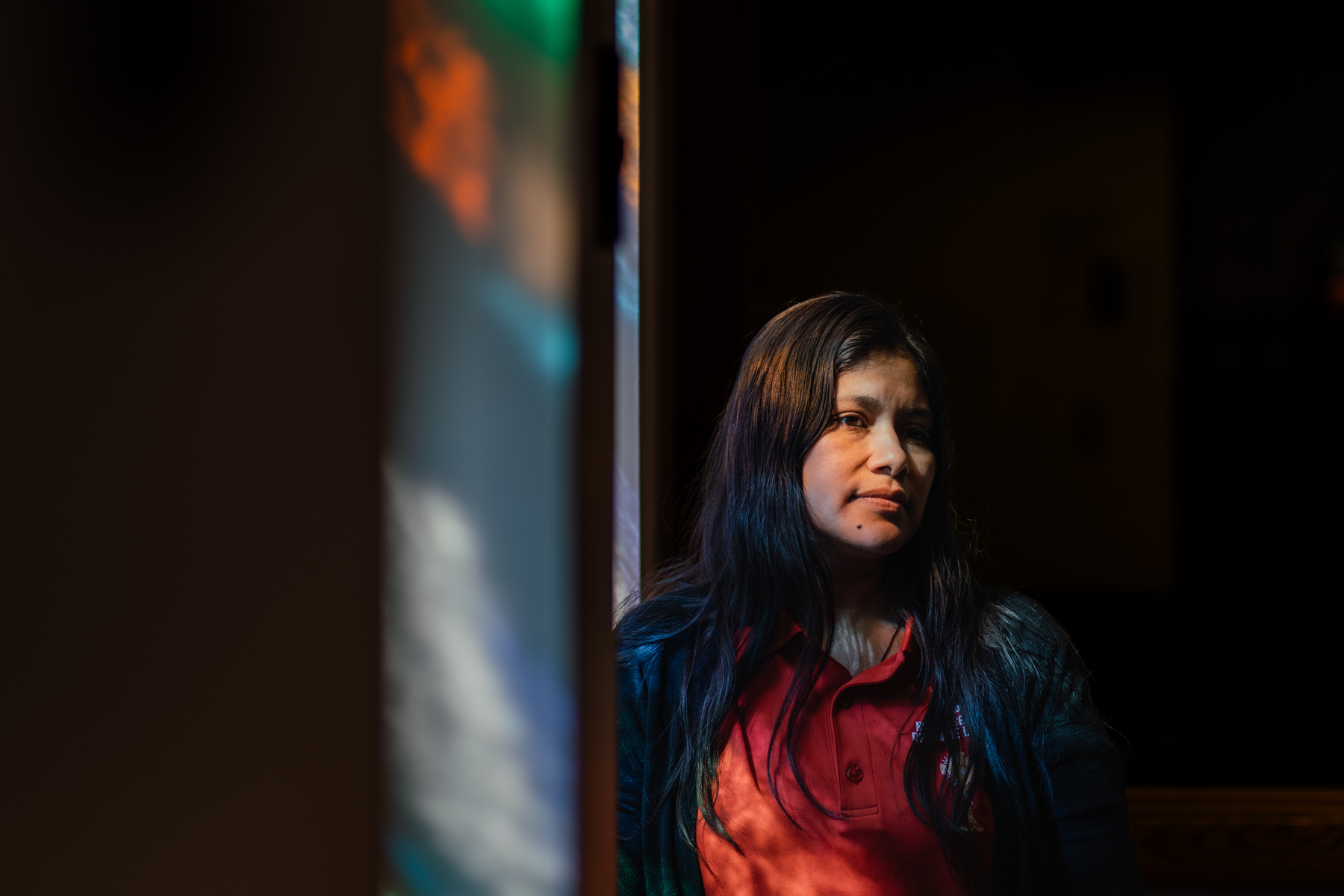 A portrait of a woman whose face is lit up by light through a church stained glass window.