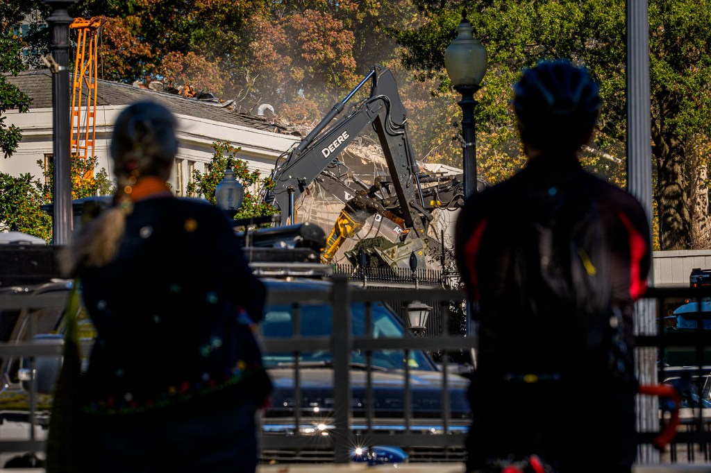 Pedestrians stop to watch the facade of the East Wing of the White House being demolished by work crews.