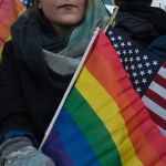 People hold signs and flags at a rally in front of the Stonewall Inn in solidarity with immigrants, asylum seekers, refugees, and the LGBT community.