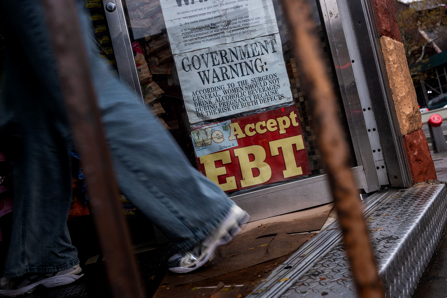 A person walks into a corner store displaying a large sign in the window that reads “We Accept EBT.”