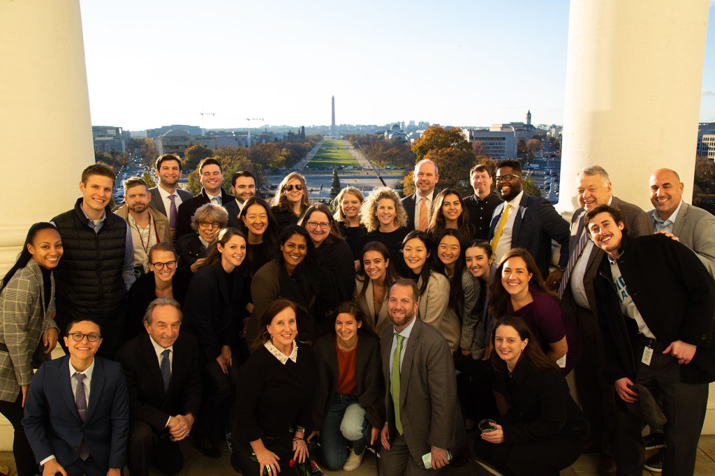 A large group of Pelosi staffers pose together on an outdoor balcony with the National Mall visible in the background. Terri McCullough is in the front row, third from the left. The Washington Monument and the Capitol grounds can be seen in the distance.
