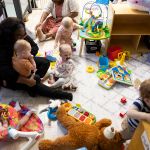 Babies play alongside two caregivers in a childcare center.