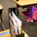A single book bag hangs off an empty chair in a classroom.