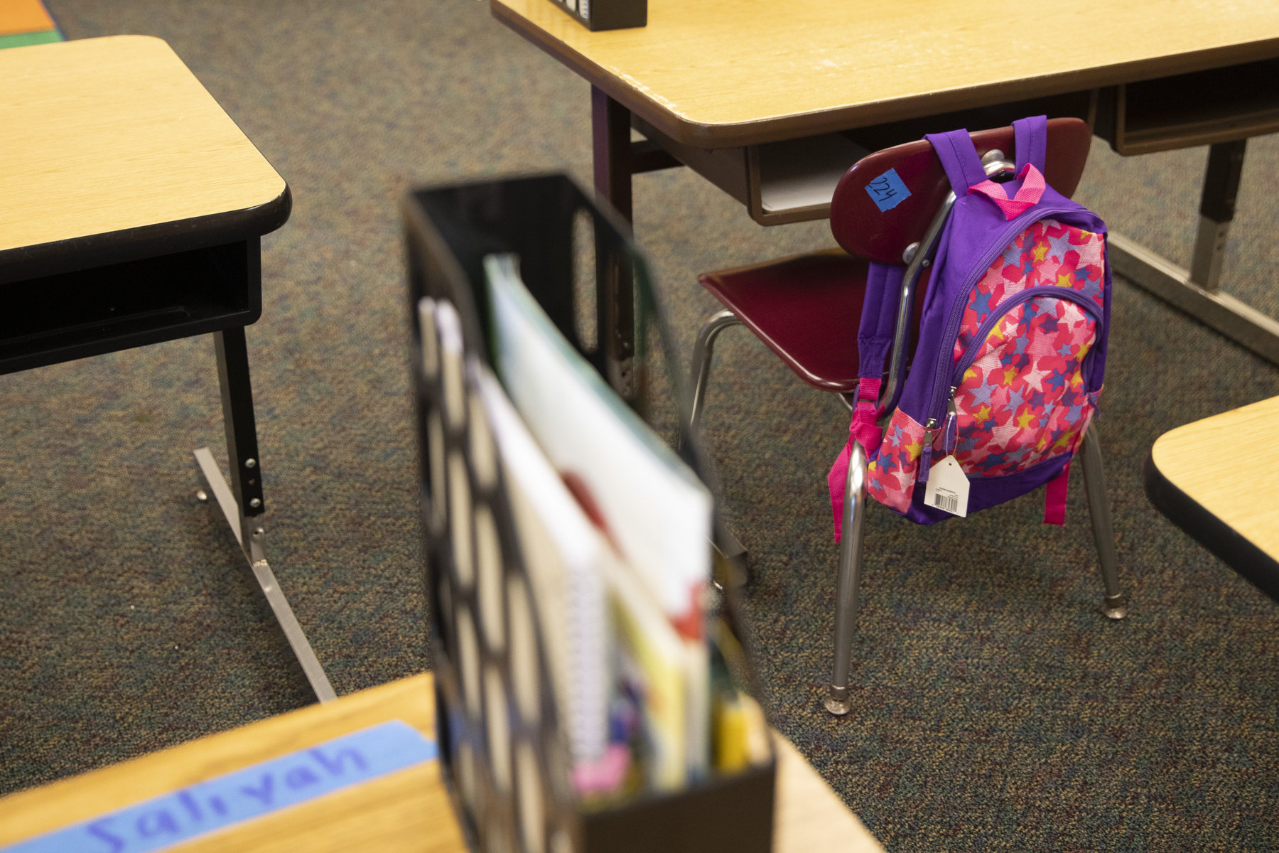 A single book bag hangs off an empty chair in a classroom.