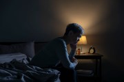 Older Asian woman sitting on a bed with a night light on.