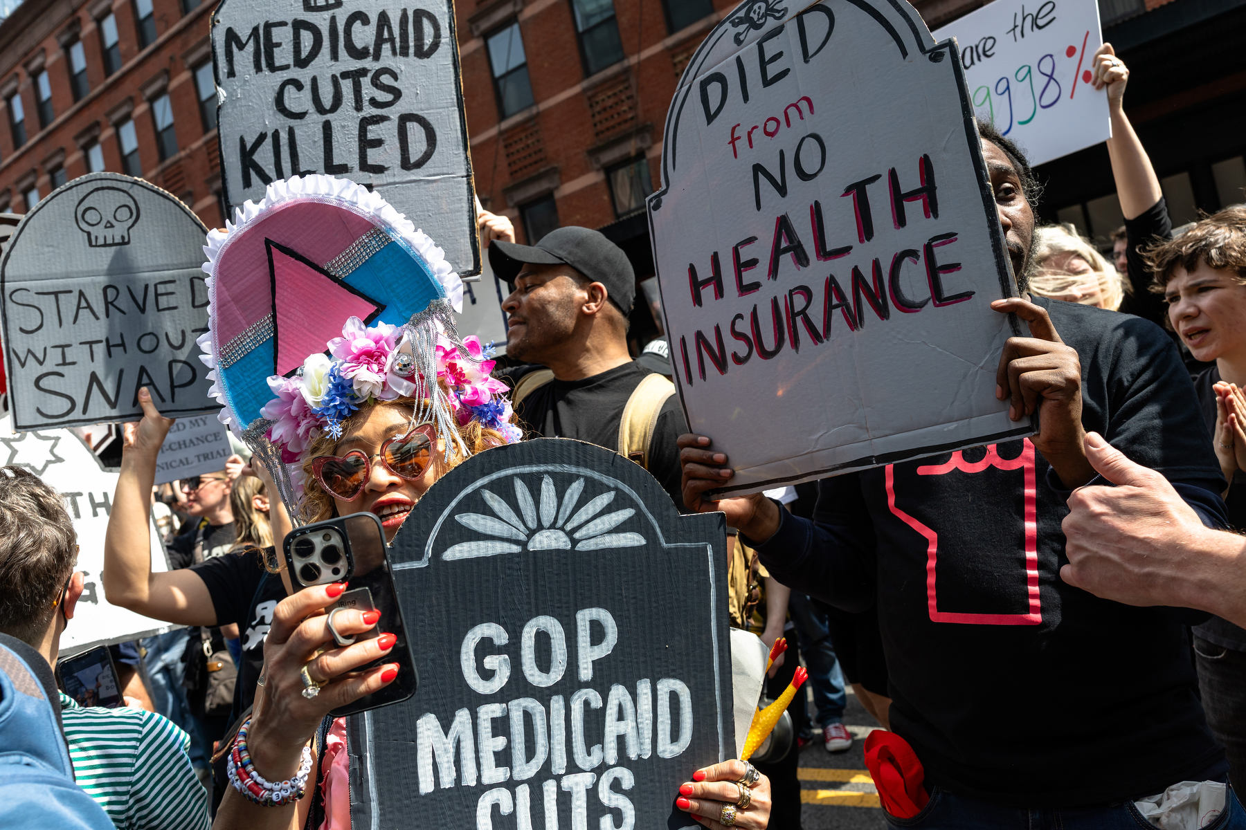 People hold signs saying "died from health insurance" and trans symbolism.