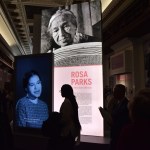 A young person is silhouetted by a lit-up exhibit of Rosa Parks in the Library of Congress.