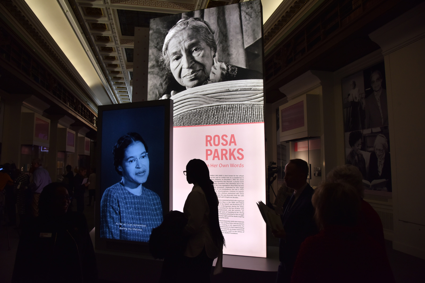 A young person is silhouetted by a lit-up exhibit of Rosa Parks in the Library of Congress.
