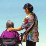 Digital collage of a person standing beside an older adult seated in a wheelchair places a hand on the seated person’s shoulder.