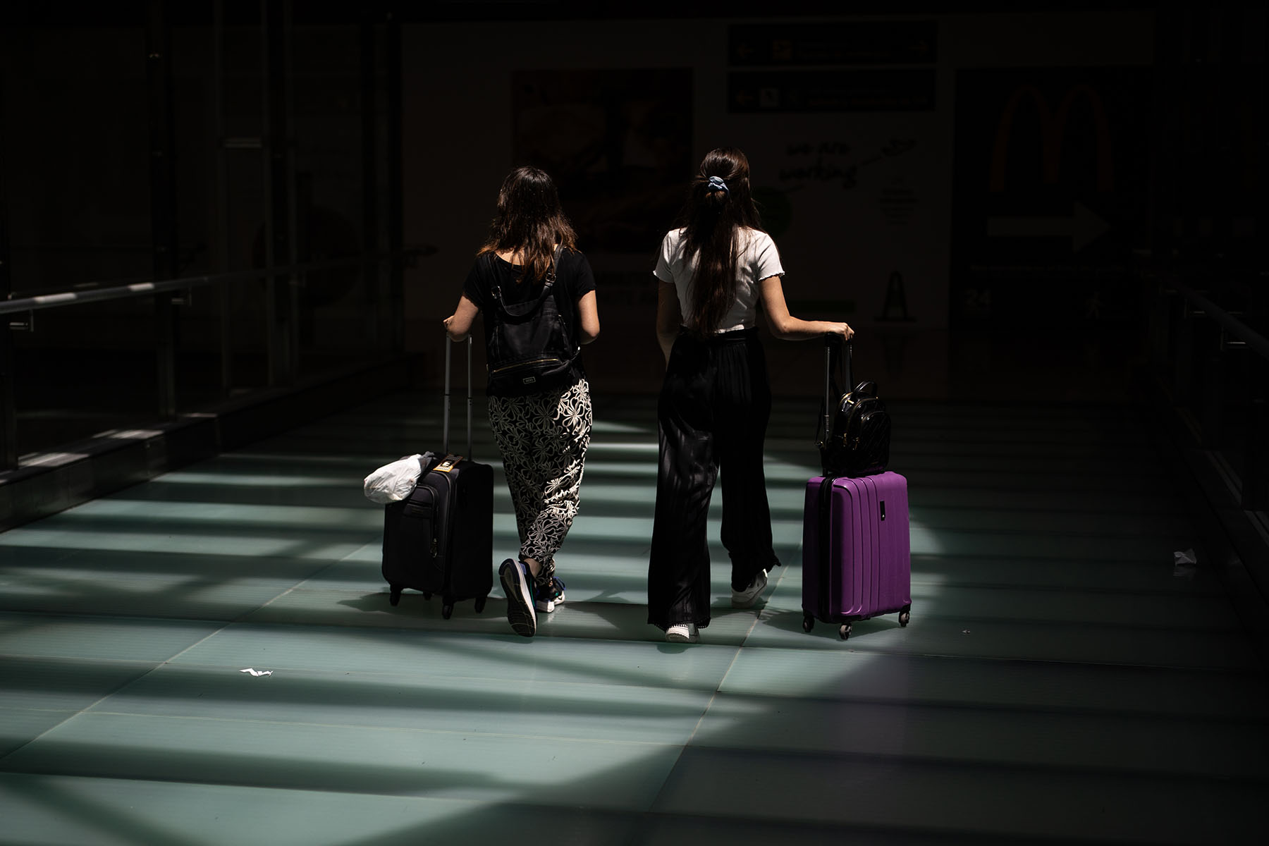 Two women with suitcases walk through an airport.