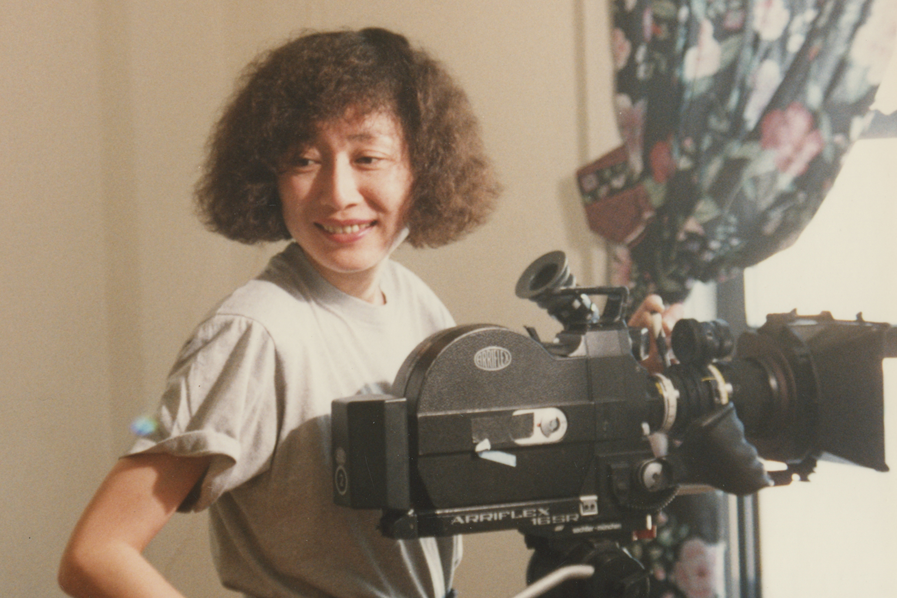 Filmmaker Christine Choy behind the scenes making a film, standing beside a film camera.