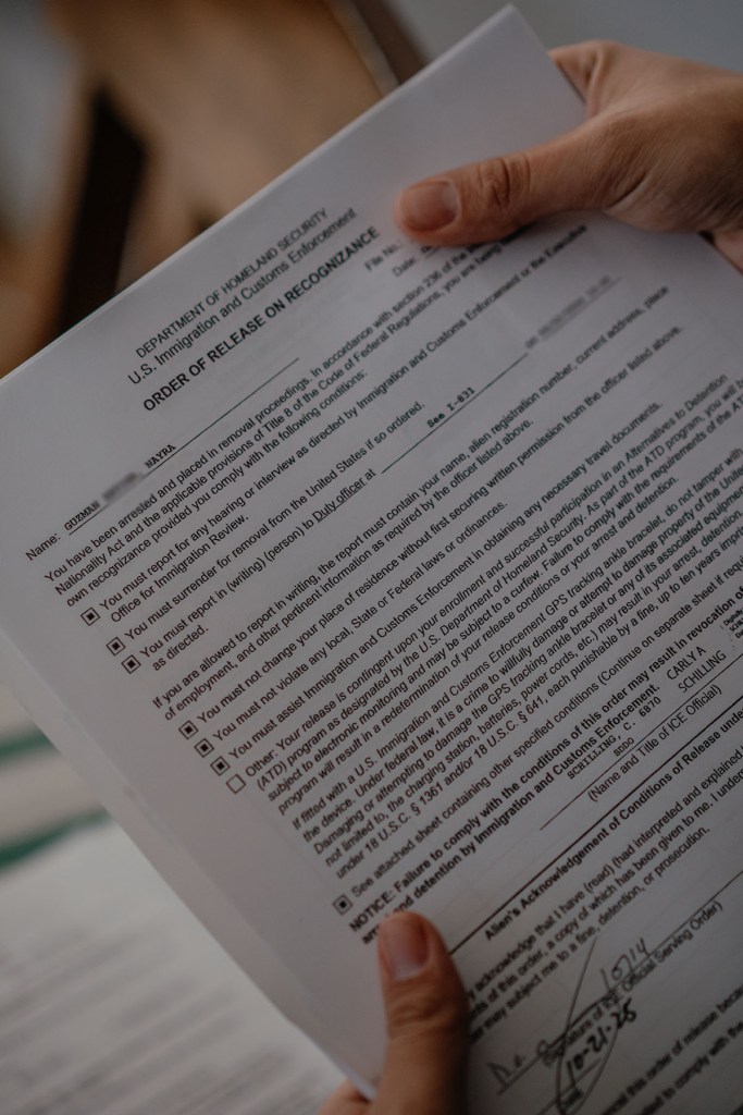 Hands holding ICE release documents with printed conditions of release.