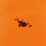 A few dark red drops of blood scattered across a bright orange textile.