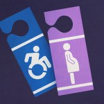 A blue disability parking placard and a purple placard with an icon of a pregnant person hang next to each other against a dark background.