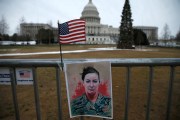 A flag and a poster showing Babbitt's military portrait is taped to a fence outside the Capitol.