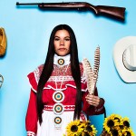 An image of an Indigenous woman wearing and surrounded by symbols of her tribal culture, photographed within a life-size box made to look like a doll’s box.