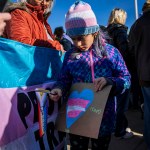 A child holds a sign with a heart in the colors of the trans pride flag.