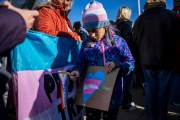 A child holds a sign with a heart in the colors of the trans pride flag.
