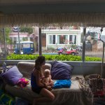 A woman holds a baby in a messy home as she looks out the window.