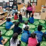 Two AKA members read to a classroom of young children.