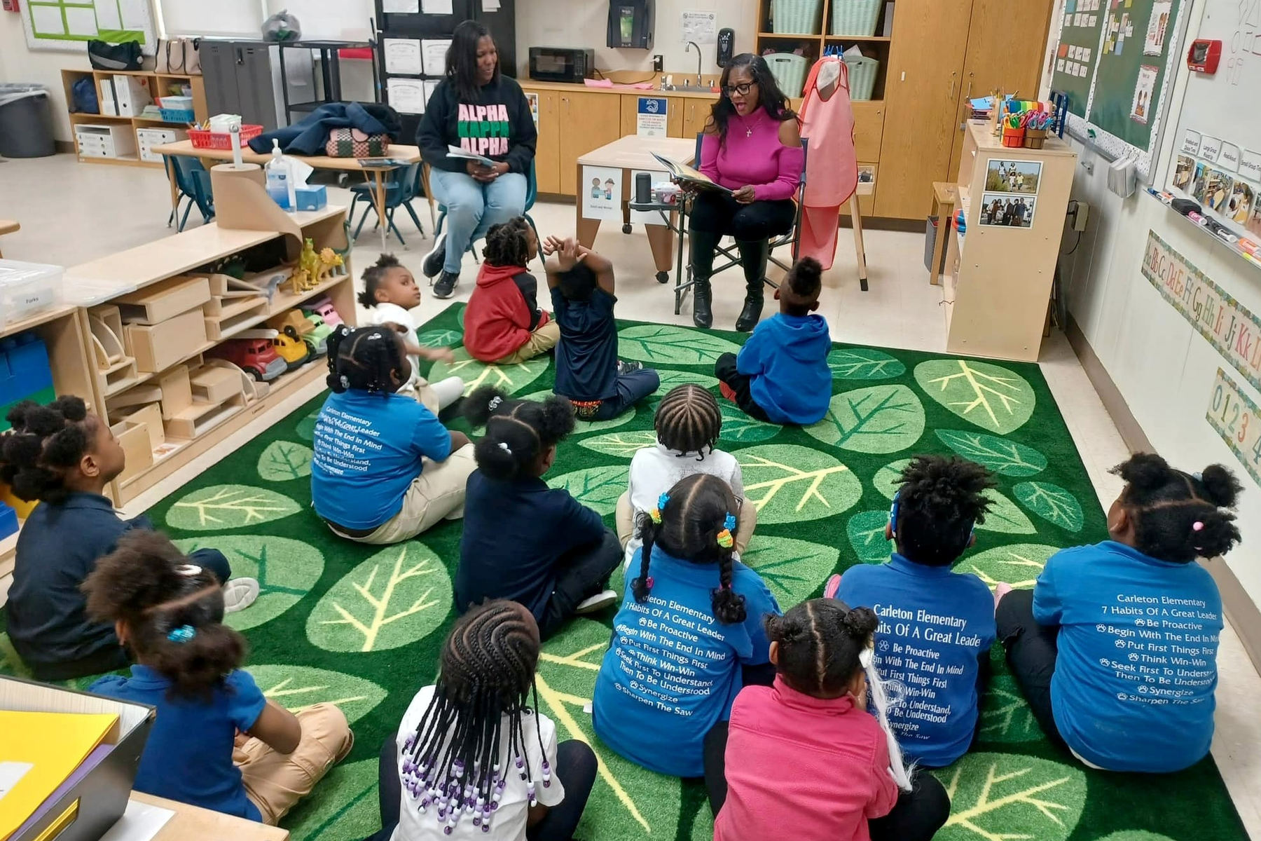 Two AKA members read to a classroom of young children.