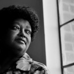 Black-and-white portrait of Claudette Colvin in April 1998, seated near a window and looking off to the side.