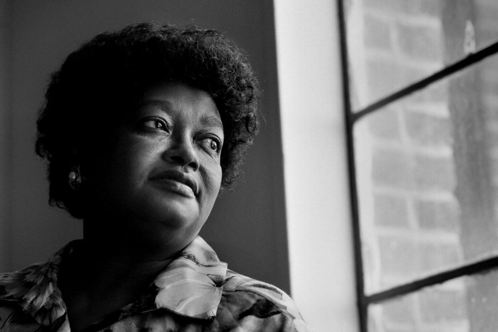 Black-and-white portrait of Claudette Colvin in April 1998, seated near a window and looking off to the side.