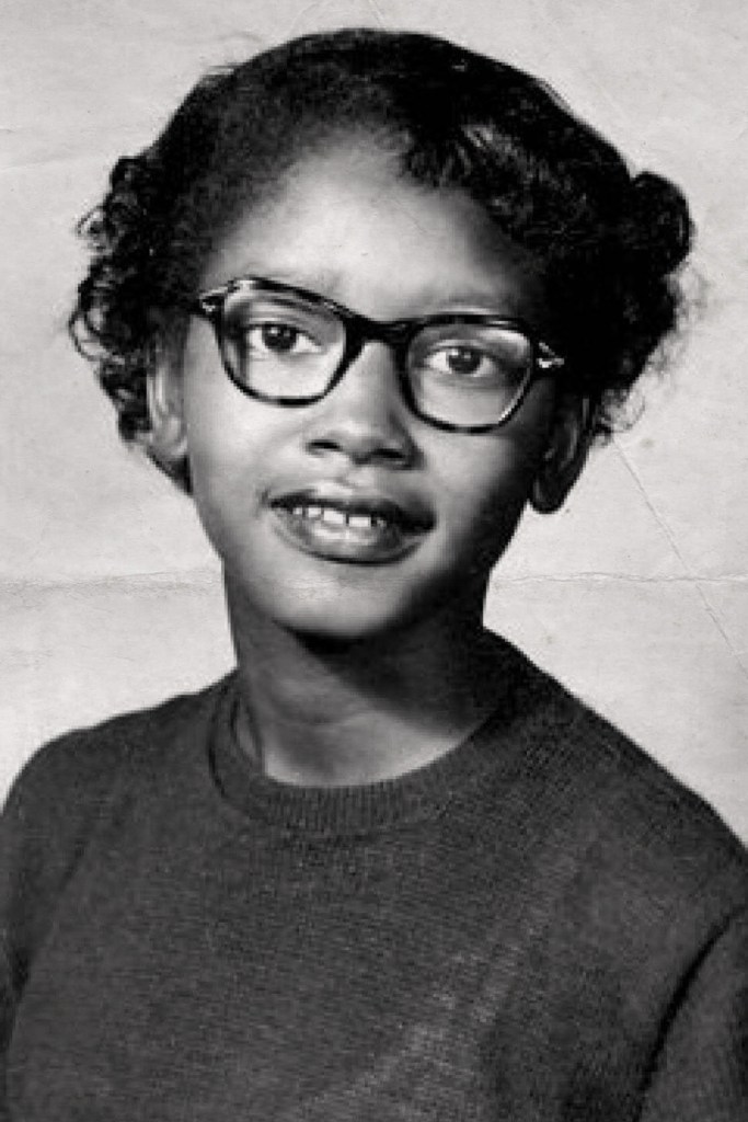 Black-and-white portrait of a young Claudette Colvin wearing glasses, looking directly at the camera.
