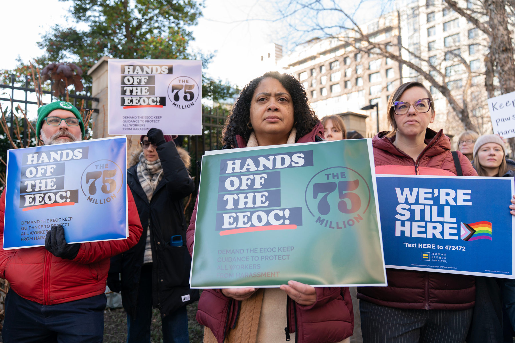 People hold signs in protest while standing in a group.