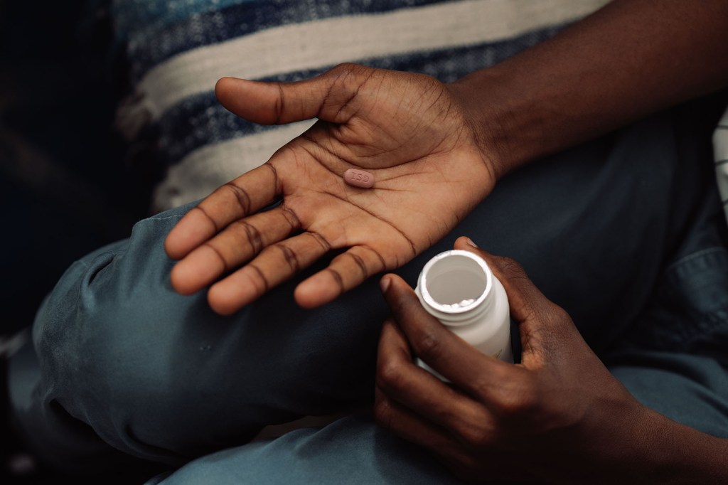 A close-up of a person’s hands, one open and the other holding a pill bottle. A single pill rests in the open palm.
