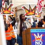 Nekima Levy Armstrong speaks at a podium with a raised fist as thousands rally for the nationwide No Kings day of protest against the Trump administration.