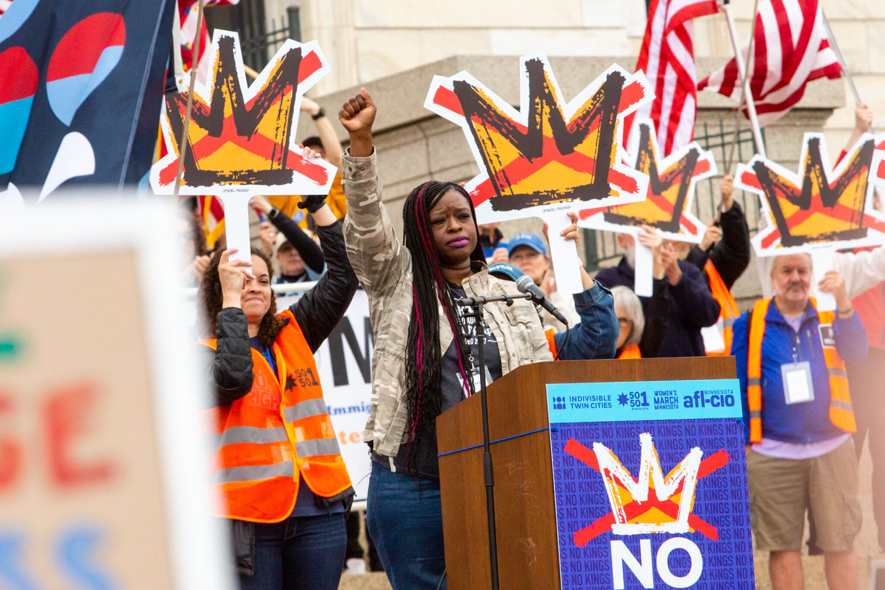 Nekima Levy Armstrong speaks at a podium with a raised fist as thousands rally for the nationwide No Kings day of protest against the Trump administration.